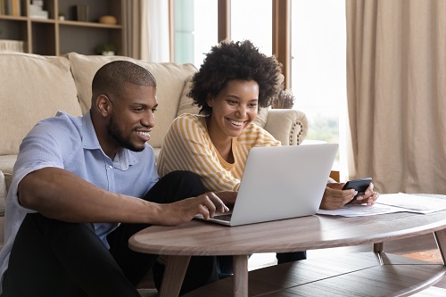 african american couple sitting at computer with calculator to pay off debt