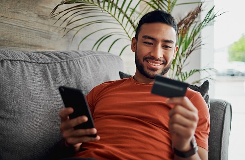 man entering debit card info into phone happy and relaxed